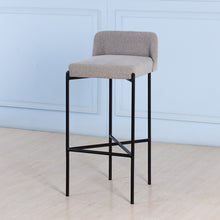 Load image into Gallery viewer, Bar stool with gray cushioned seat and black metal frame against a light blue wall.
