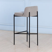 Load image into Gallery viewer, Bar stool with gray cushioned seat and black metal frame against a light blue wall.