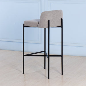 Bar stool with gray cushioned seat and black metal frame against a light blue wall.
