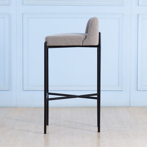 Bar stool with gray cushioned seat and black metal frame against a light blue paneled wall.