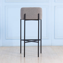 Load image into Gallery viewer, Bar stool with gray cushioned seat and black metal frame against a light blue wall.
